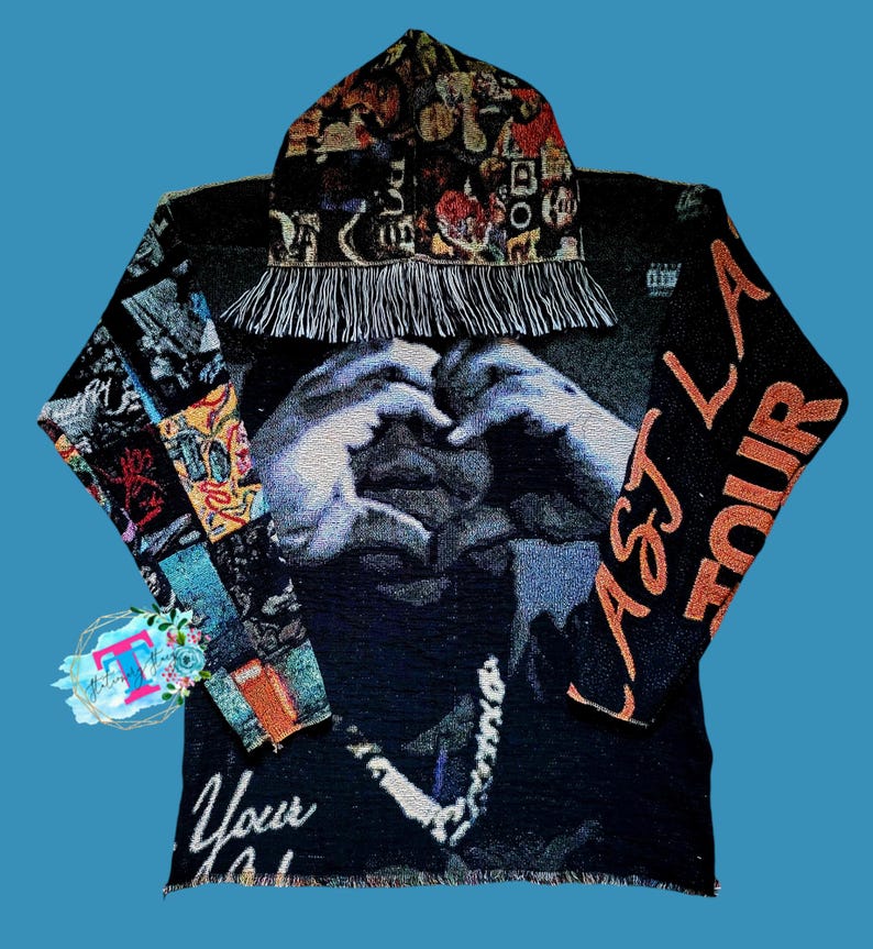 May include: Black hooded sweatshirt with a colorful tapestry design featuring a person making a heart shape with their hands. The sweatshirt has the text "Astroworld" on the right sleeve and "Your" on the bottom left corner.