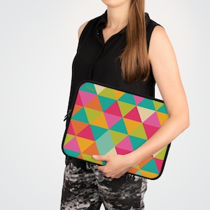 May include: A colorful laptop sleeve featuring a geometric pattern of triangles in shades of pink, orange, yellow, green, and teal. The sleeve has a black border and a zipper closure. The sleeve is being held by a person.