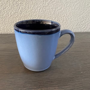 May include: A light blue ceramic mug with a dark blue rim. The mug has a rounded shape and a handle.