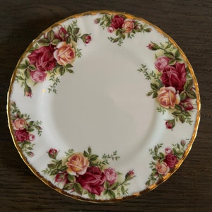 May include: A white porcelain plate with a gold rim and a floral design featuring red, pink, and yellow roses. The plate has a scalloped edge.