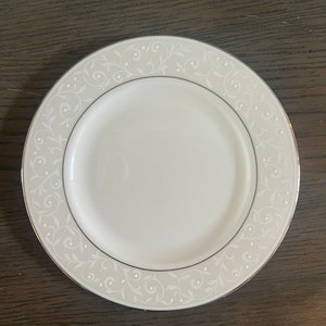 May include: White ceramic plate with a silver rim and a delicate floral pattern.