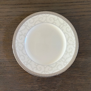 May include: A white ceramic saucer with a silver and gray floral pattern.