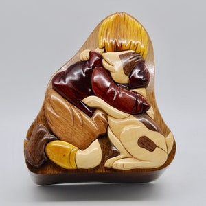 May include: A wooden puzzle box with a carved design of a child hugging a dog. The box is made of different types of wood, including light brown, dark brown, and red.