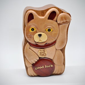 以下が含まれることがあります： 持ち上げられた足、赤い首輪、そして胸に「福」の漢字が書かれた木製の猫の置物。猫は「幸運」と書かれた丸い木製の円盤を持っています。