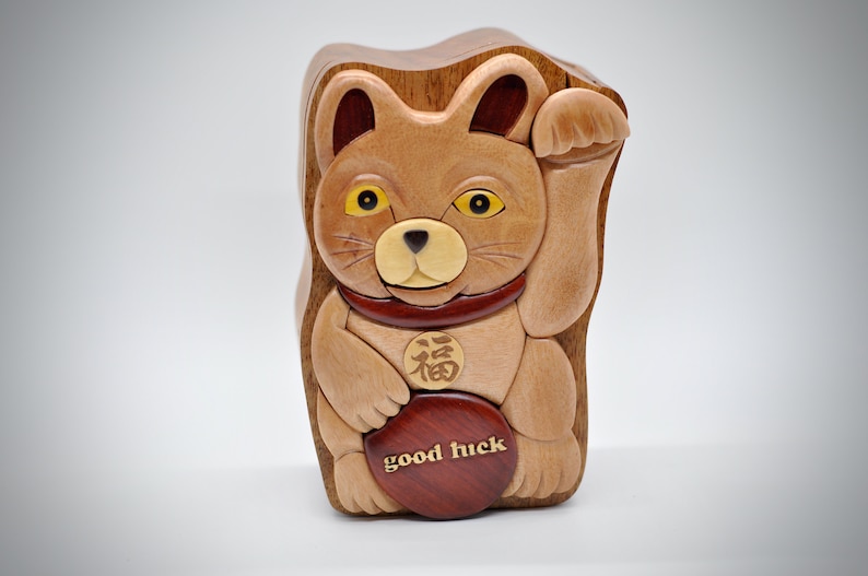 以下が含まれることがあります： 持ち上げられた足、赤い首輪、そして胸に「福」の漢字が書かれた木製の猫の置物。猫は「幸運」と書かれた丸い木製の円盤を持っています。