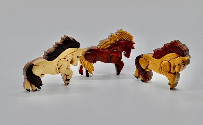 K&ouml;nnte beinhalten: Drei h&ouml;lzerne Pferdefiguren, jede aus einem anderen Holz geschnitzt. Die Pferde sind in einer springenden Pose, mit ihren M&auml;hnen und Schw&auml;nzen, die hinter ihnen wehen.