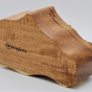 Op de afbeelding: Een houten doos met een unieke, organische vorm. De doos is gemaakt van lichtbruin hout met een natuurlijk houtnerfpatroon. De doos is gesloten en heeft een klein, gegraveerd logo aan de voorkant met de tekst "WooderVie".