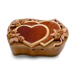 May include: A wooden heart-shaped puzzle box with intricate carvings of flowers and leaves. The box is made of light and dark wood, creating a beautiful contrast.