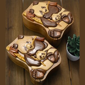 Puede incluir: Dos cajas de rompecabezas de madera talladas intrincadamente con forma de pandas. Las cajas est&aacute;n hechas de madera clara y oscura, creando un efecto contrastante. Cada caja presenta una madre panda sosteniendo un beb&eacute; panda. Las cajas son una adici&oacute;n &uacute;nica y decorativa a cualquier hogar.