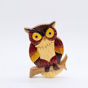 May include: A wooden owl figurine with intricate details, carved from different colored woods. The owl is perched on a branch and has a realistic appearance.