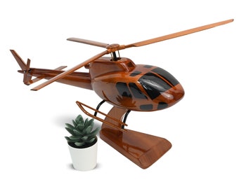 Könnte beinhalten: Ein Holzmodell eines braunen Hubschraubers mit schwarzen Akzenten. Der Hubschrauber steht auf einem Holzsockel und hat neben sich eine kleine grüne Pflanze in einem weißen Topf.
