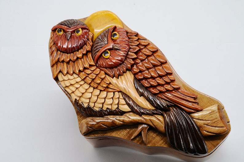 Op de afbeelding: Een houten uil puzzeldoos met ingewikkelde details. De doos heeft twee uilen die op een tak zitten, met een halve maan erboven. De uilen zijn gesneden met realistische veren en ogen, en de doos is afgewerkt in een rijke bruine kleur.