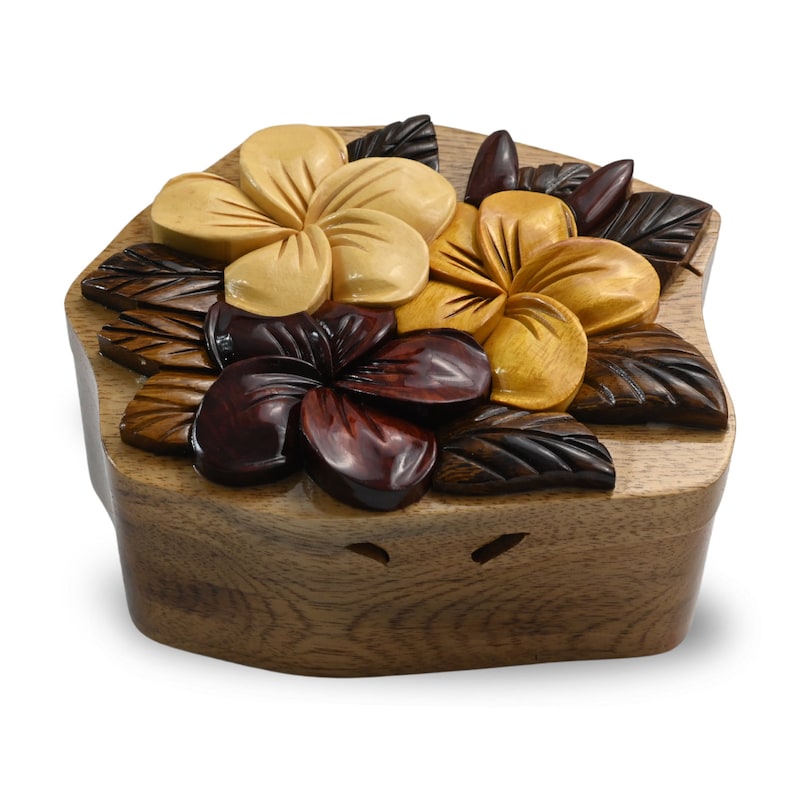 May include: A wooden puzzle box featuring a carved design of three plumeria flowers in shades of brown, yellow, and red. The box is closed and has a smooth, polished finish.