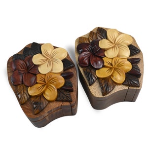 May include: Two intricately carved wooden puzzle boxes with a floral design. The boxes are made of dark wood and feature a variety of colours, including brown, red, and yellow. The boxes are closed and have a unique shape.
