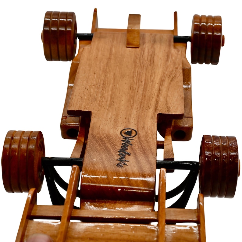 Puede incluir: Un coche de carreras de juguete de madera con ruedas negras y un logotipo "Woodcraft" en la parte inferior. El coche est&aacute; hecho de madera marr&oacute;n claro y tiene un dise&ntilde;o detallado.