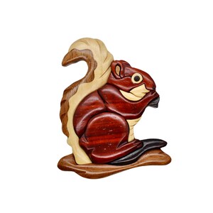May include: A wooden squirrel figurine with a detailed, layered design. The squirrel is primarily reddish-brown with lighter wood accents on the tail, face, and belly. It appears to be holding a nut. The figurine is mounted on a wooden base.