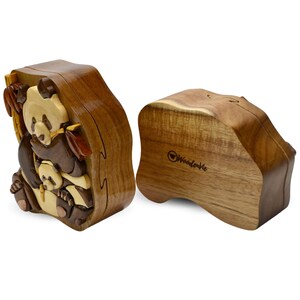Puede incluir: Una caja de rompecabezas de madera con un dise&ntilde;o de oso panda tallado. La caja est&aacute; hecha de madera marr&oacute;n claro y tiene una tapa con bisagras. La caja est&aacute; abierta y el interior es visible. La caja est&aacute; hecha por WoodenWe.