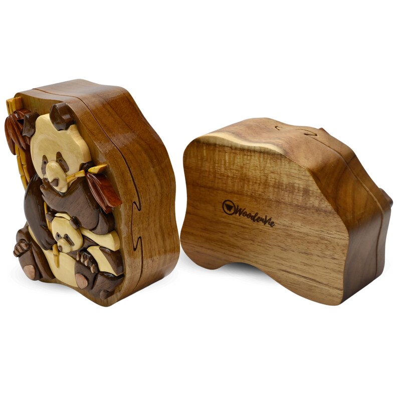 Puede incluir: Una caja de rompecabezas de madera con un dise&ntilde;o de oso panda tallado. La caja est&aacute; hecha de madera marr&oacute;n claro y tiene una tapa con bisagras. La caja est&aacute; abierta y el interior es visible. La caja est&aacute; hecha por WoodenWe.