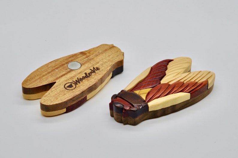 Puede incluir: Un im&aacute;n de madera con forma de cigarra con detalles intrincados y una variedad de tonos de madera. La parte posterior del im&aacute;n presenta el logotipo "Woodenvue" y un im&aacute;n plateado.