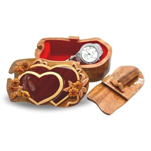 May include: A wooden puzzle box with a heart design and intricate carvings. The box is open and a watch is inside. The box has a separate lid that is also carved with a heart design.