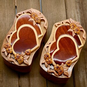 May include: Two intricately carved wooden heart-shaped boxes with a natural wood finish. The boxes are decorated with floral designs and have a glossy finish.