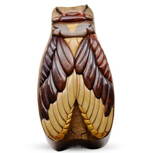May include: A wooden puzzle box shaped like a cicada with intricate details. The wings are made of different shades of brown and cream wood. The box is closed and has a hinged lid.