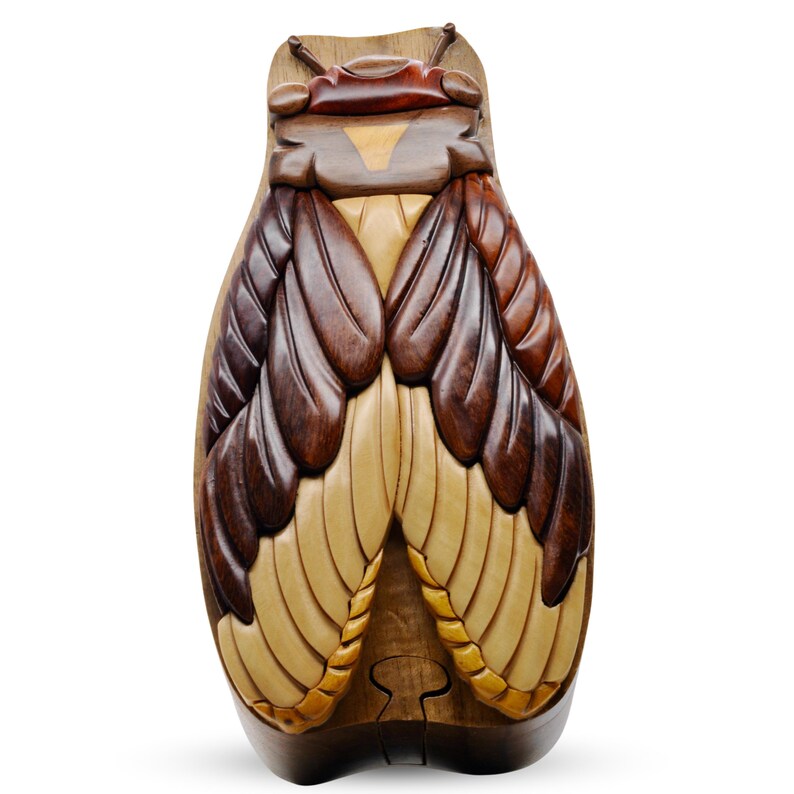 May include: A wooden puzzle box shaped like a cicada with intricate details. The wings are made of different shades of brown and cream wood. The box is closed and has a hinged lid.