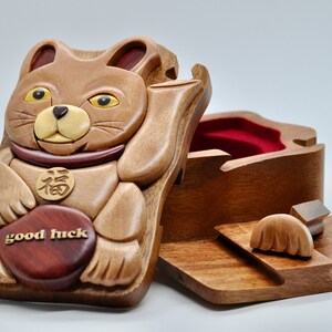 以下が含まれることがあります： 「幸運」と刻まれた赤いハートを持った茶色の猫の形をした木製パズルボックス。猫は、中国語の文字が書かれた金の首輪をしている。箱は開いており、内側は赤いベルベットで覆われている。