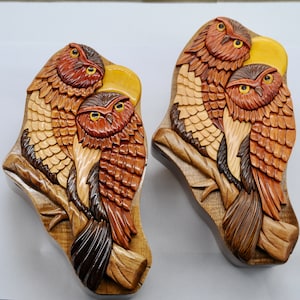 Op de afbeelding: Twee ingewikkeld gesneden houten puzzeldozen in de vorm van uilen. Elke doos heeft drie uilen met bruine, oranje en gele veren, die op een tak zitten. De dozen zijn gemaakt van lichtbruin hout met een natuurlijke afwerking.