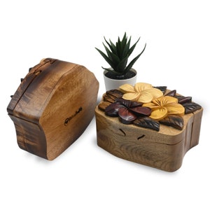 May include: Two wooden puzzle boxes with intricate carvings of flowers. The box on the right has a floral design with yellow, orange, and red flowers. The box on the left is closed and has a simple design.