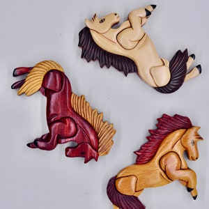 K&ouml;nnte beinhalten: Drei Holzpferde-Figuren, jede in einer anderen Farbe geschnitzt. Eine ist hellbraun, eine dunkelbraun und eine rotbraun. Die Pferde sind alle in verschiedenen Posen.