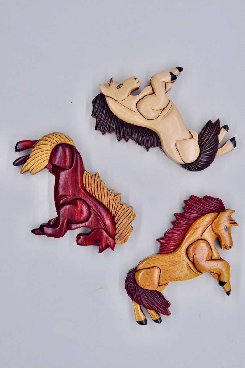 K&ouml;nnte beinhalten: Drei Holzpferde-Figuren, jede in einer anderen Farbe geschnitzt. Eine ist hellbraun, eine dunkelbraun und eine rotbraun. Die Pferde sind alle in verschiedenen Posen.