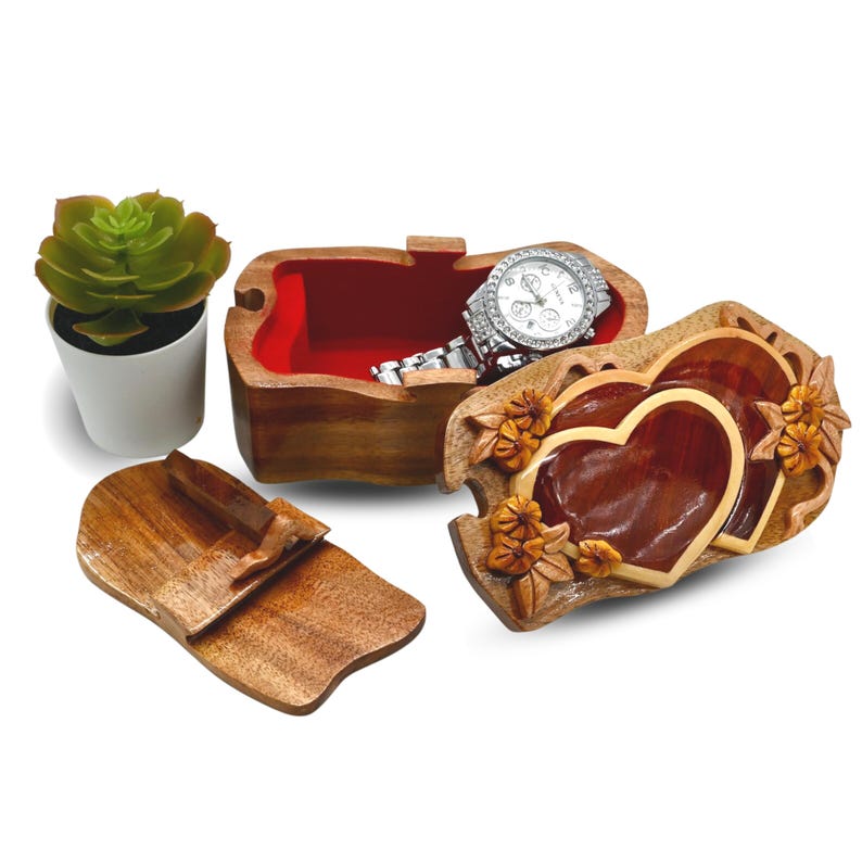 May include: A wooden puzzle box with a red interior and a carved design of two hearts with flowers. The box is open and a watch is inside.