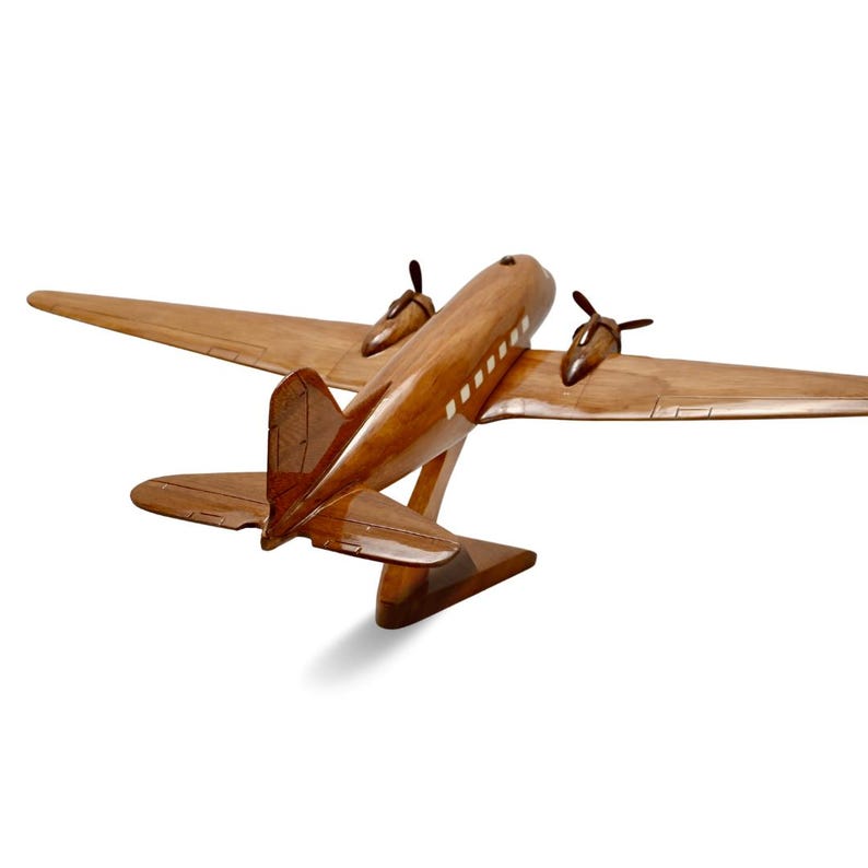 K&ouml;nnte beinhalten: Ein Holzmodell eines Vintage-Flugzeugs mit braunem Holz und wei&szlig;en Akzenten. Das Modell steht auf einem Holzst&auml;nder und wird von hinten betrachtet.