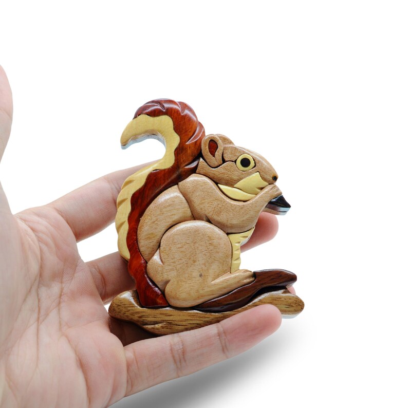 May include: A wooden squirrel figurine with a detailed design. The squirrel is made of various wood tones, including light brown, dark brown, and red. It is holding a nut and has a bushy tail. The figurine is approximately 4 inches tall.