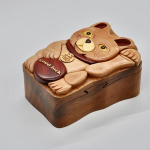 以下が含まれることがあります： 猫の形をした木製のパズルボックス。赤い金色のコインが入っています。クルミ材で作られており、猫の顔と足が細かく彫刻されています。箱には「幸運」と刻まれています。