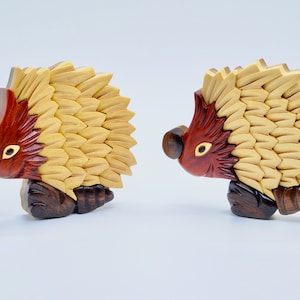 May include: Two wooden hedgehogs with intricate details. The hedgehogs are carved from wood and painted in shades of brown, red, and yellow. The hedgehogs are facing each other and have a playful expression.