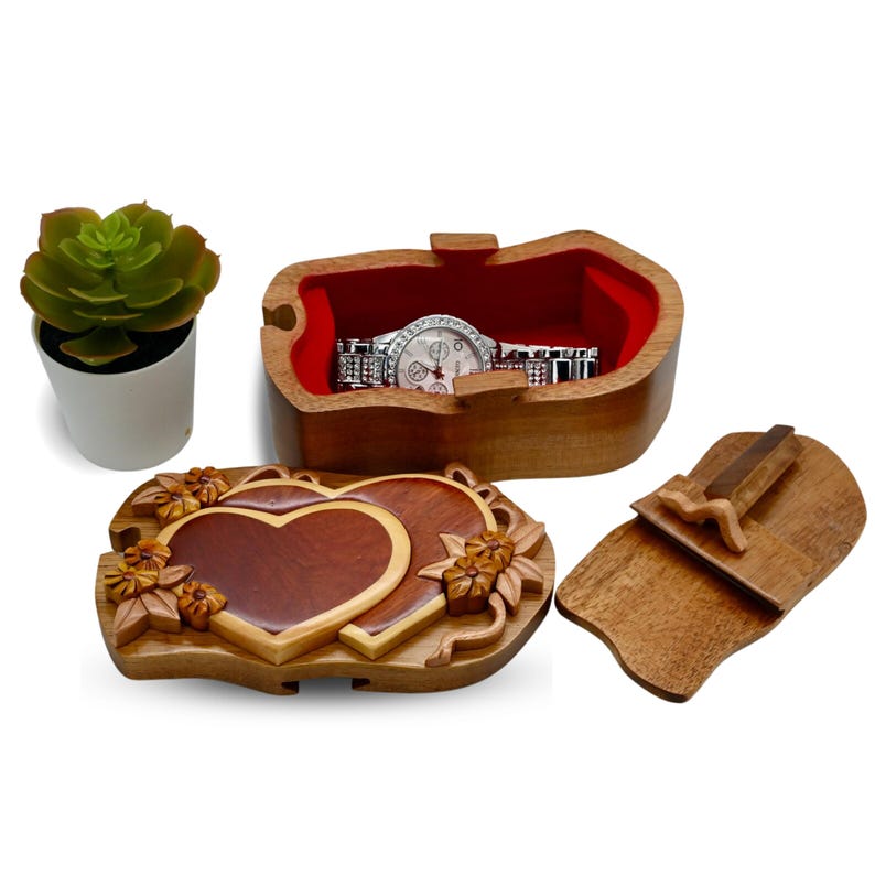 May include: A wooden puzzle box with a heart-shaped lid. The box is made of light and dark wood and has a red velvet interior. The lid is carved with two hearts and floral details. The box is open and a watch is inside.