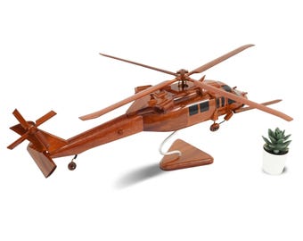 Könnte beinhalten: Ein handgefertigtes Holzmodell eines Hubschraubers in einem satten, rotbraunen Finish. Das Modell verfügt über detaillierte Rotorblätter, einen Heckrotor und einen Ständer. Eine kleine Sukkulente in einem weißen Topf befindet sich neben dem Modell.