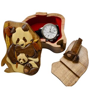 Puede incluir: Una caja de rompecabezas de madera con un dise&ntilde;o de oso panda. La caja est&aacute; abierta y hay un reloj en su interior. La caja est&aacute; hecha de madera marr&oacute;n claro y tiene un forro de fieltro rojo.