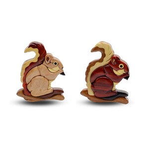 May include: Two wooden squirrel figurines, each perched on a small branch. One squirrel is light brown with a reddish-brown tail, the other is dark brown with a reddish-brown tail. Both have black beaks and are set against a white background.