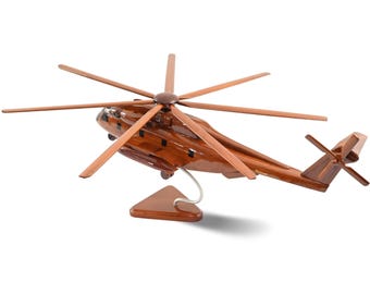 Könnte beinhalten: Ein detailliertes Holzmodell eines Hubschraubers mit einem dunkelbraunen Rumpf und hellbraunen Rotorblättern. Das Modell ist auf einem Holzständer mit Metallstütze montiert. Das Design zeigt die komplizierten Details des Flugzeugs.