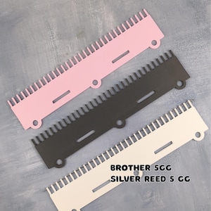 May include: Three knitting machine needle selectors in pink, black, and white. Each has a series of teeth along one edge, a hole, and a slot. The text "BROTHER 5CG SILVER REED 5 CG" is printed on the white selector.
