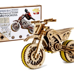 May include: Wooden model kit of a motocross motorcycle. The motorcycle is made of wood and has a yellow and black color scheme. The kit includes all the parts needed to assemble the motorcycle. The box shows a rider on a similar motorcycle.