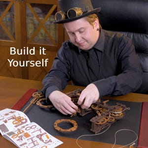 May include: A person assembling a wooden mechanical model with gears and other components. The model is brown and appears to be a clockwork mechanism. The text "Build it Yourself" is visible in the image.