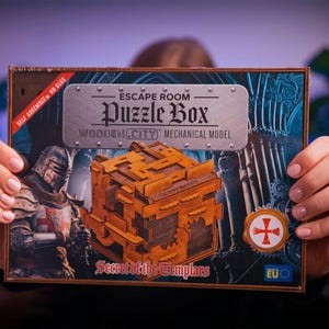 Może przedstawiać: Drewniana skrzynia z zagadkami o tematyce średniowiecznej. Skrzynia jest brązowa i ma metalową płytkę z przodu z napisem "Escape Room Puzzle Box Wooden City Mechanical Model Secret of the Templars".