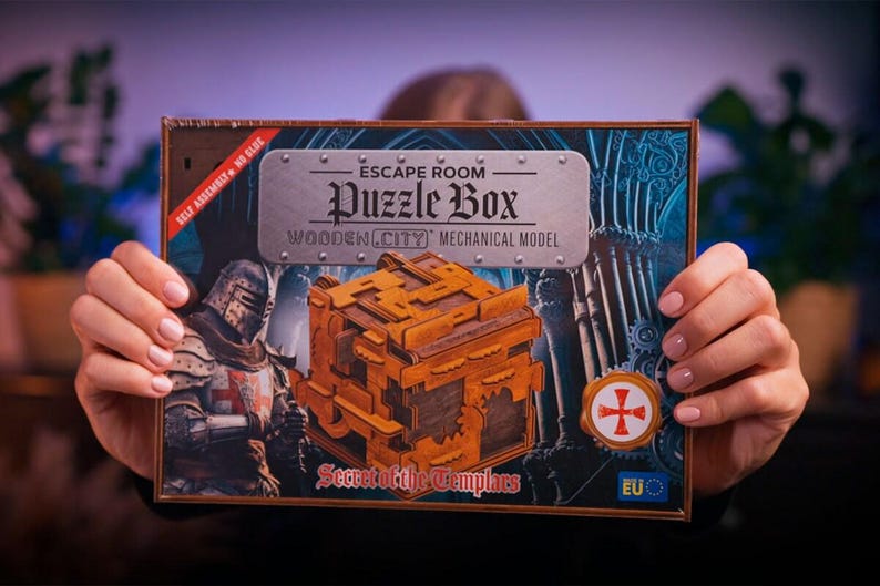 Może przedstawiać: Drewniana skrzynia z zagadkami o tematyce średniowiecznej. Skrzynia jest brązowa i ma metalową płytkę z przodu z napisem "Escape Room Puzzle Box Wooden City Mechanical Model Secret of the Templars".