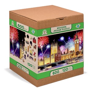 May include: A cardboard box with a green and white label featuring a 600-piece wooden jigsaw puzzle of the Houses of Parliament in London at night with fireworks. The puzzle is 120 cm x 80 cm.