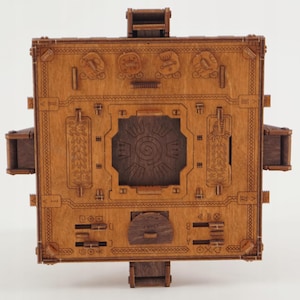 Puede incluir: Una caja de rompecabezas de madera con intrincadas tallas y un dise&ntilde;o complejo. La caja es de color marr&oacute;n c&aacute;lido y presenta varios s&iacute;mbolos, patrones y un dise&ntilde;o central en espiral. Tiene m&uacute;ltiples partes m&oacute;viles.