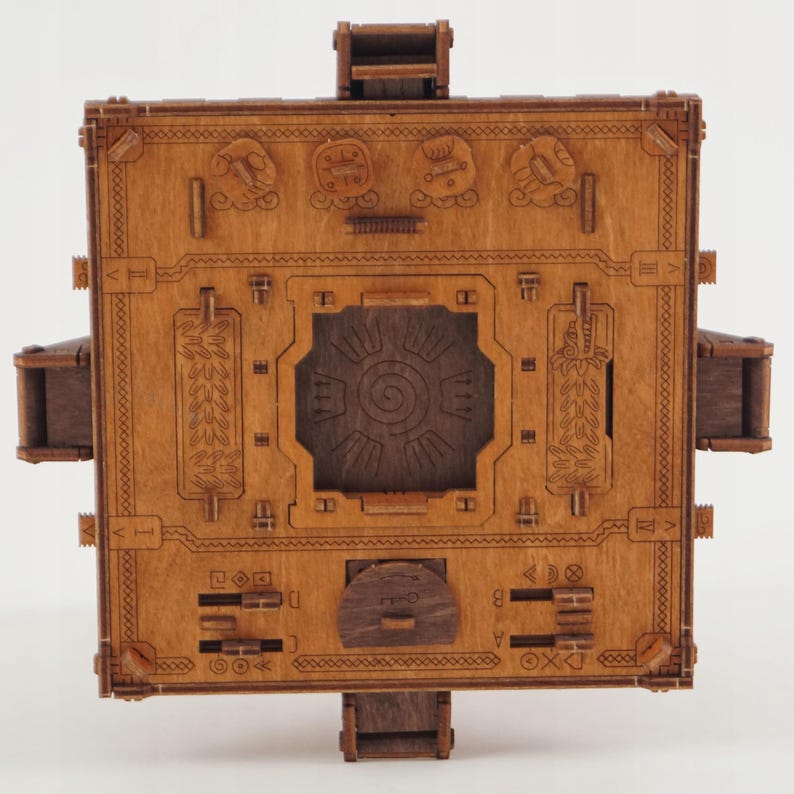 Puede incluir: Una caja de rompecabezas de madera con intrincadas tallas y un dise&ntilde;o complejo. La caja es de color marr&oacute;n c&aacute;lido y presenta varios s&iacute;mbolos, patrones y un dise&ntilde;o central en espiral. Tiene m&uacute;ltiples partes m&oacute;viles.